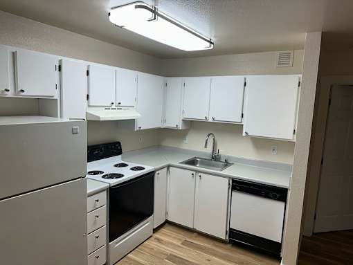 A white kitchen with a stove, sink, and cabinets.
