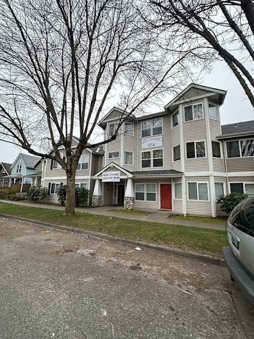 A grey house with a red door is in front of a tree.