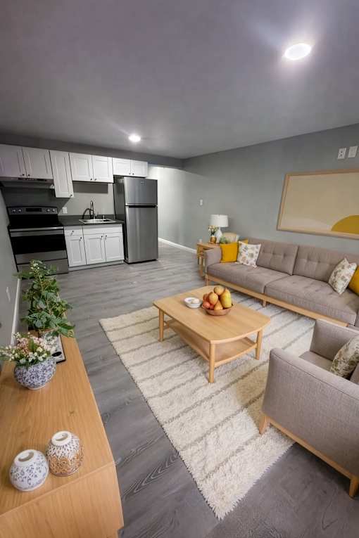 A modern living room with a grey sofa, wooden coffee table, and a kitchen area in the background.