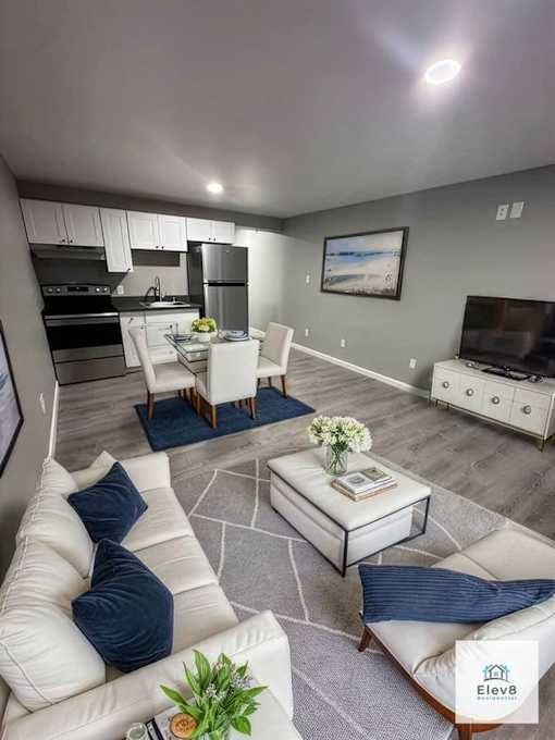 A modern living room with a kitchen area in the background.