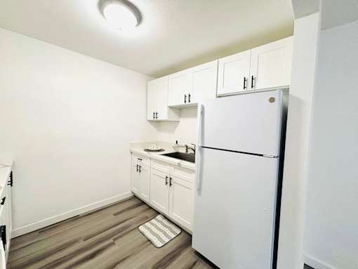 A white refrigerator is in a kitchen with white cabinets.