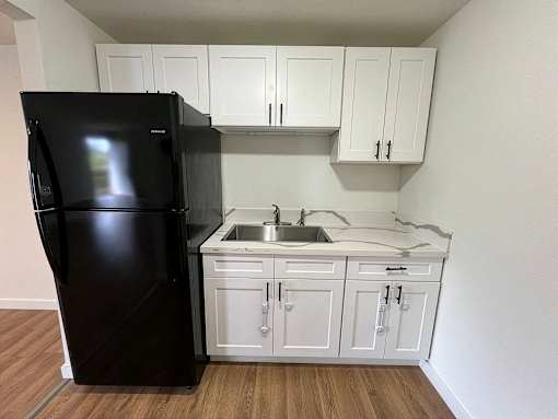 A black refrigerator is in a kitchen with white cabinets.