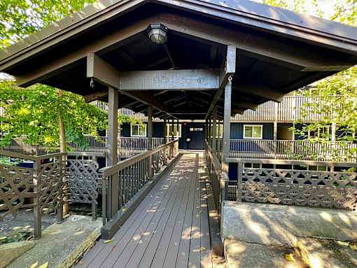 A wooden deck with a roof and railings leading to a building.