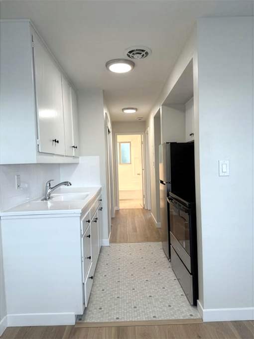 A kitchen with white cabinets and a black refrigerator.