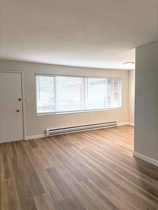 A room with a white door, a window with blinds, and a radiator on the wall.