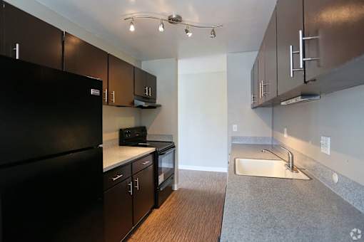 A kitchen with a black refrigerator and wooden cabinets.