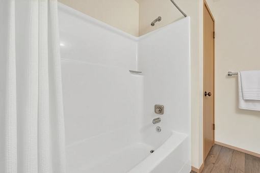 A white bathtub with a shower curtain and a towel hanging on the door.