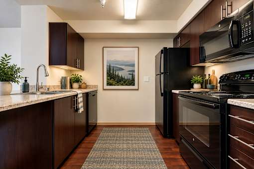 A kitchen with black appliances and a painting of a lake on the wall.