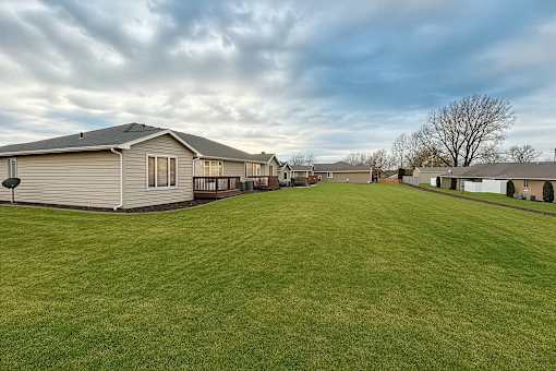 A large grassy field with a few houses in the background.