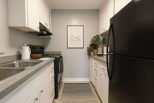 A black refrigerator sits in a kitchen with white cabinets and a grey counter.