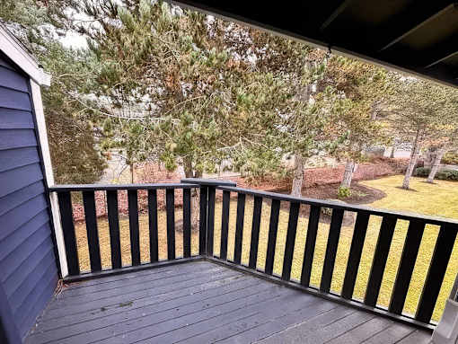 A wooden deck with a black railing overlooks a yard.