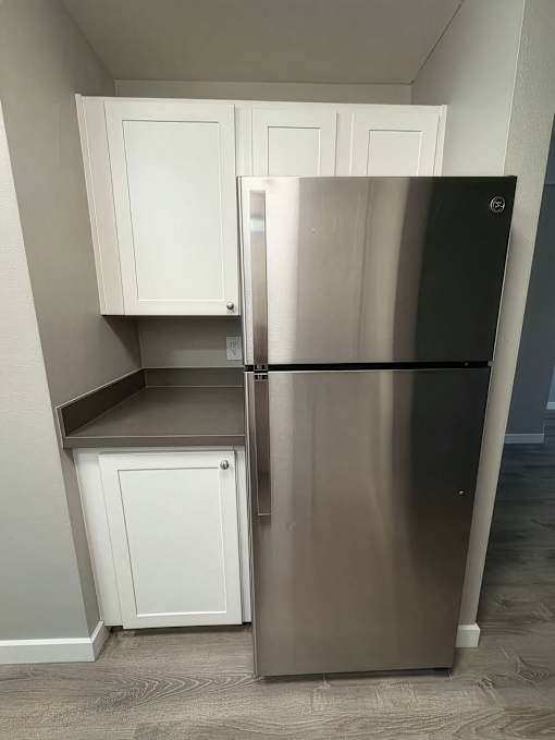 A black refrigerator in a kitchen with white cabinets.