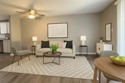A living room with a ceiling fan, a couch, a chair, a coffee table, and a bowl of fruit on the table.