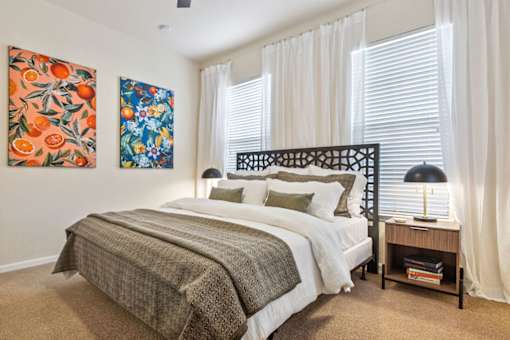 A bedroom with a bed, nightstand, and two paintings on the wall.