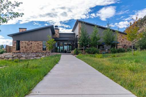 A modern building with a stone wall and a long concrete pathway leading to it.