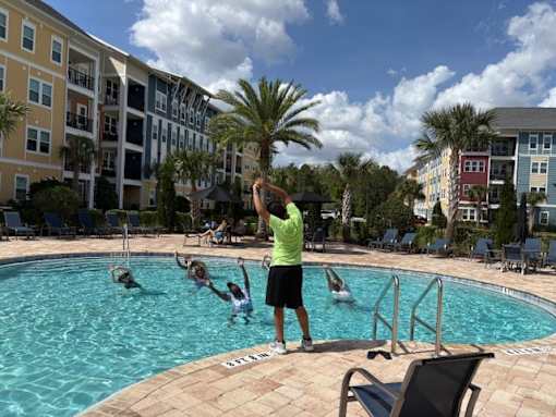 A man in a green shirt is standing by a pool with people swimming.