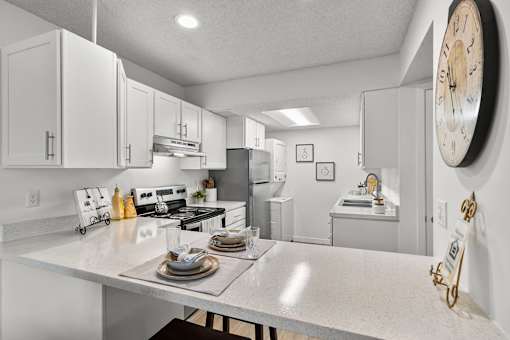 A kitchen with a table set for two and a clock on the wall.