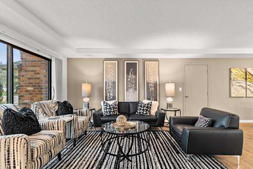 A living room with a black and white striped sofa, a black leather chair, and a coffee table with a glass top.