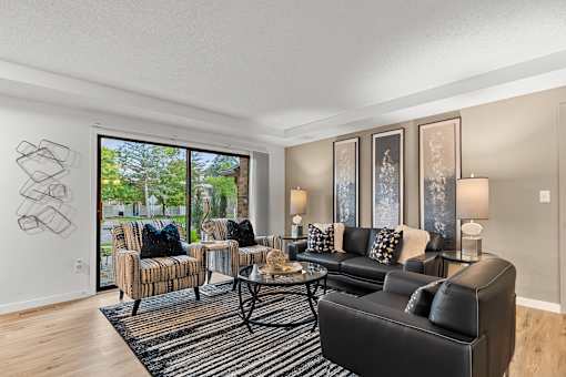 A living room with a black couch, a coffee table, and a large window.