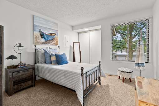 A bedroom with a bed, nightstand, and a window with a view of trees.