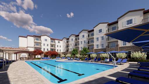 A large swimming pool is surrounded by sun loungers and apartment buildings.