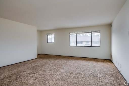 A room with a carpeted floor and two windows.
