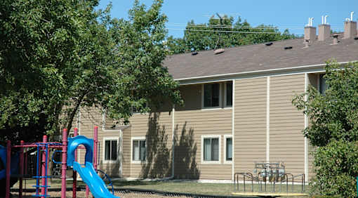 A playground with a blue slide in front of a beige house.