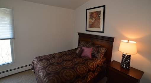 A bedroom with a bed, lamp, and picture on the wall.