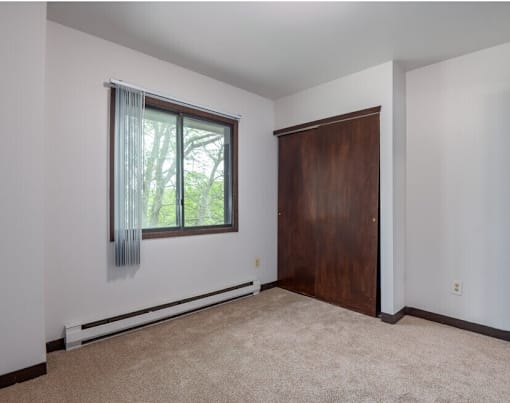 A room with a brown door and a window with a view of trees.