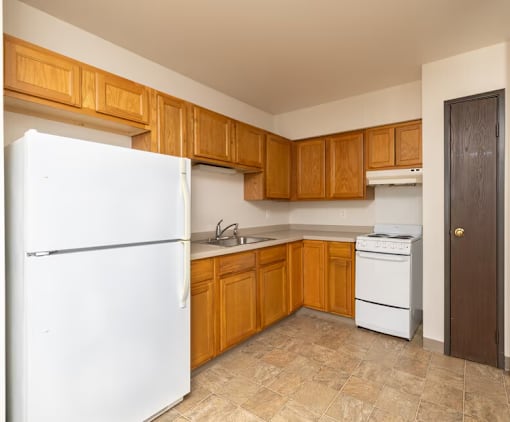 A kitchen with a white refrigerator, wooden cabinets, and a white dishwasher.