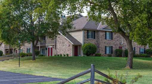 A house with a red door and green shutters is surrounded by a grassy lawn and trees.