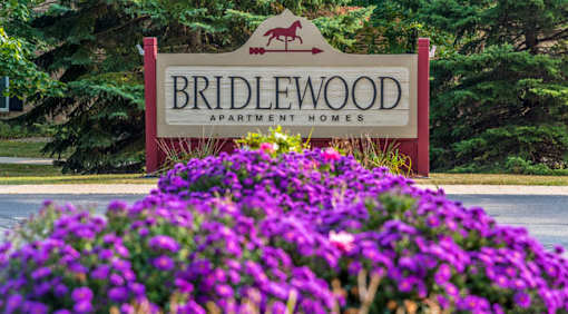 A sign for Bridlewood Apartment Homes is surrounded by purple flowers.