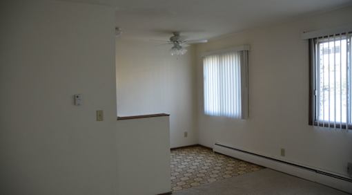 A room with a ceiling fan and two windows.