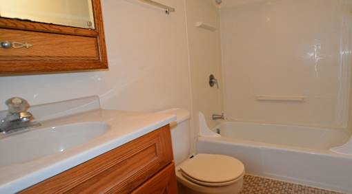 A white sink with a wooden cabinet and a toilet in a bathroom.