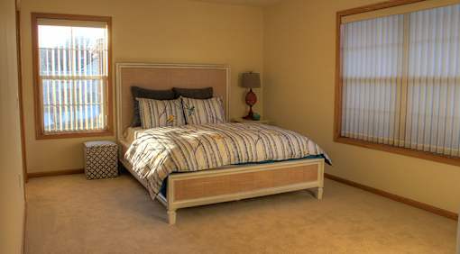 A bed with a striped comforter sits in a room with a window on the left.