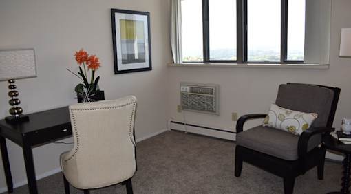 A room with a chair and a table with a vase of flowers on it.