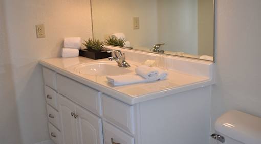 A white bathroom with a sink, mirror, and toilet.