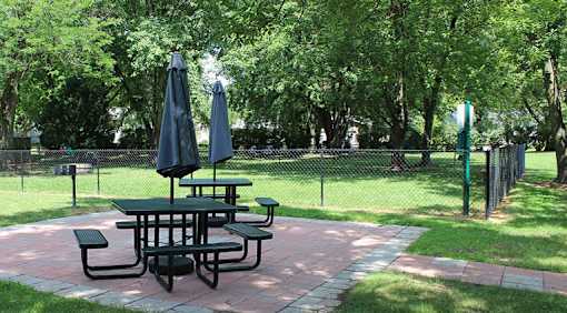 A picnic table with two umbrellas is in the middle of a park.