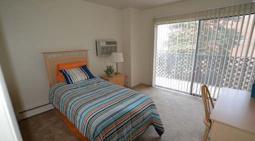 A bedroom with a bed, desk, and window with blinds.