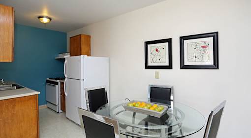 A kitchen with a white refrigerator and a glass table with two chairs and two framed pictures on the wall.