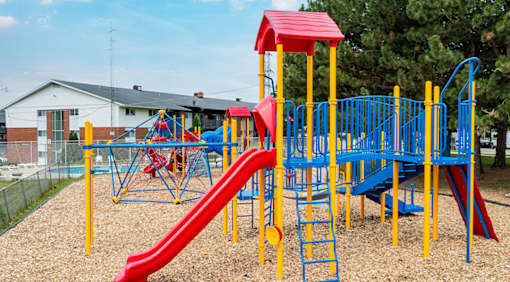 A playground with a red and blue slide and yellow safety bars.