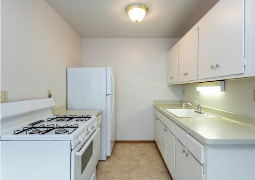 A white kitchen with a stove, refrigerator, and cabinets.