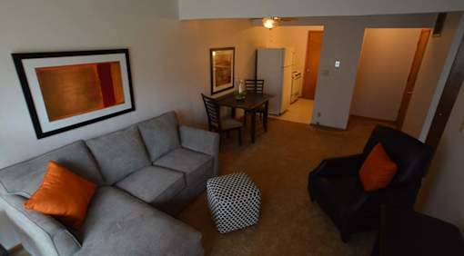 A living room with a grey couch, a black chair, and a painting on the wall.