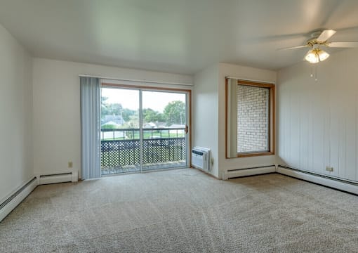A room with a carpeted floor, a ceiling fan, and a sliding glass door leading to a balcony.
