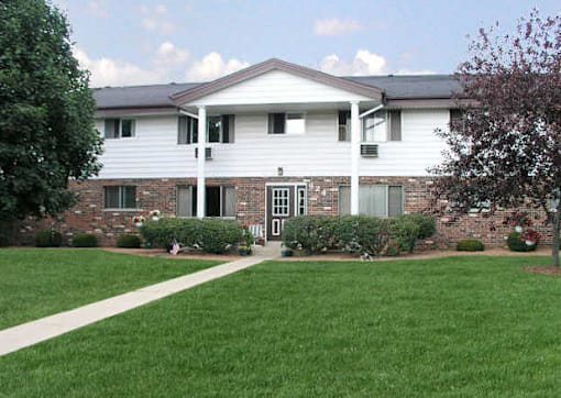 A white house with a brick wall and a green lawn in front.