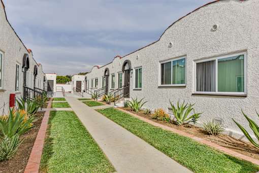 A row of white houses with green plants in front.