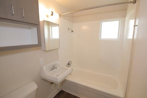 A white bathroom with a tub, sink, and mirror.