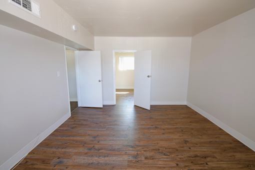 A room with wooden floors and white walls with three doors.
