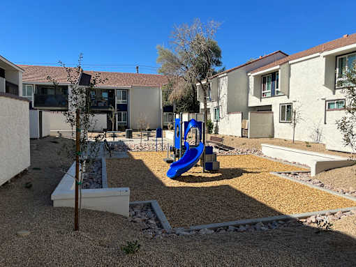 A playground with a blue slide in the middle of a gravel area.