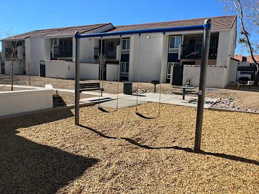 A playground with a swing set in front of a building.